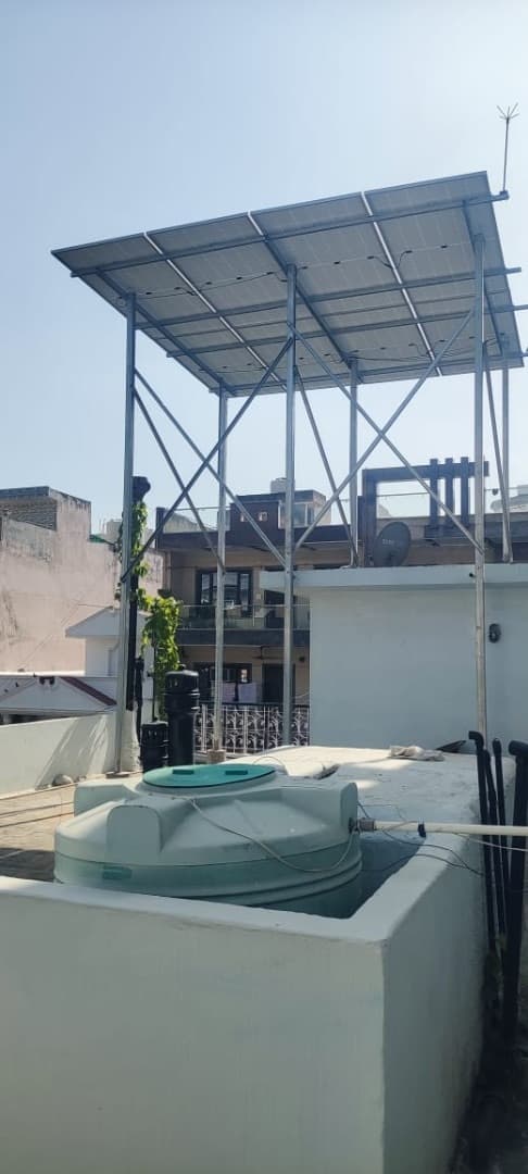 Solar panels on a tall steel frame above a house rooftop, with a water tank in the foreground