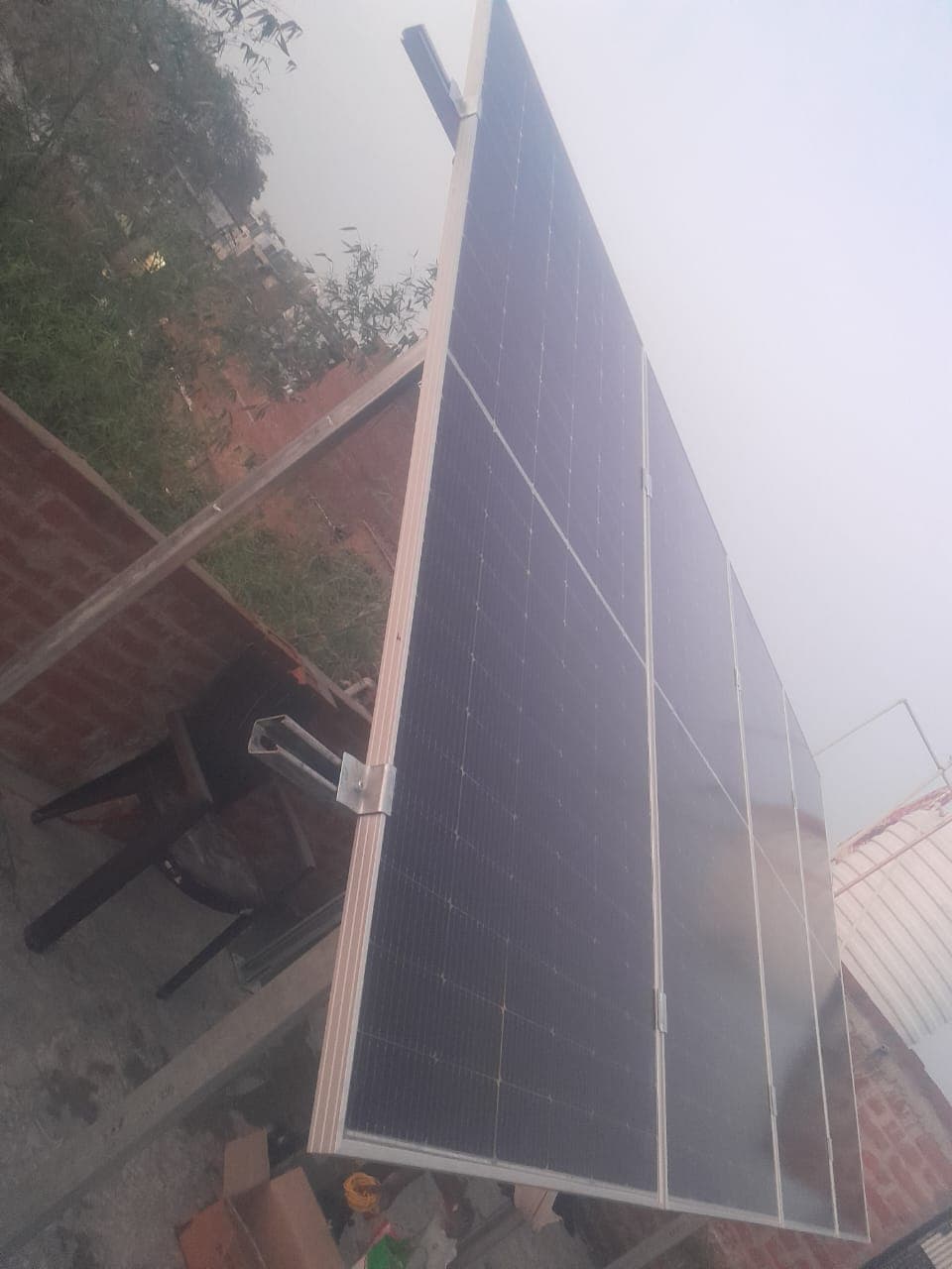 Four solar panels on a raised metal frame on a house roof, with a water tank and trees behind them